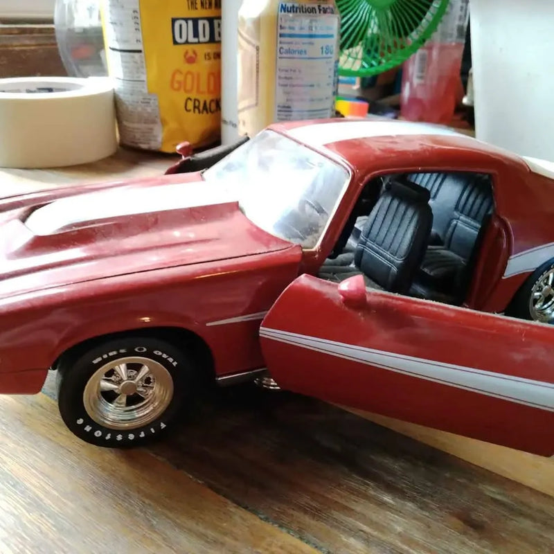 Red diecast 1970-style Camaro model car with open driver door and black seats