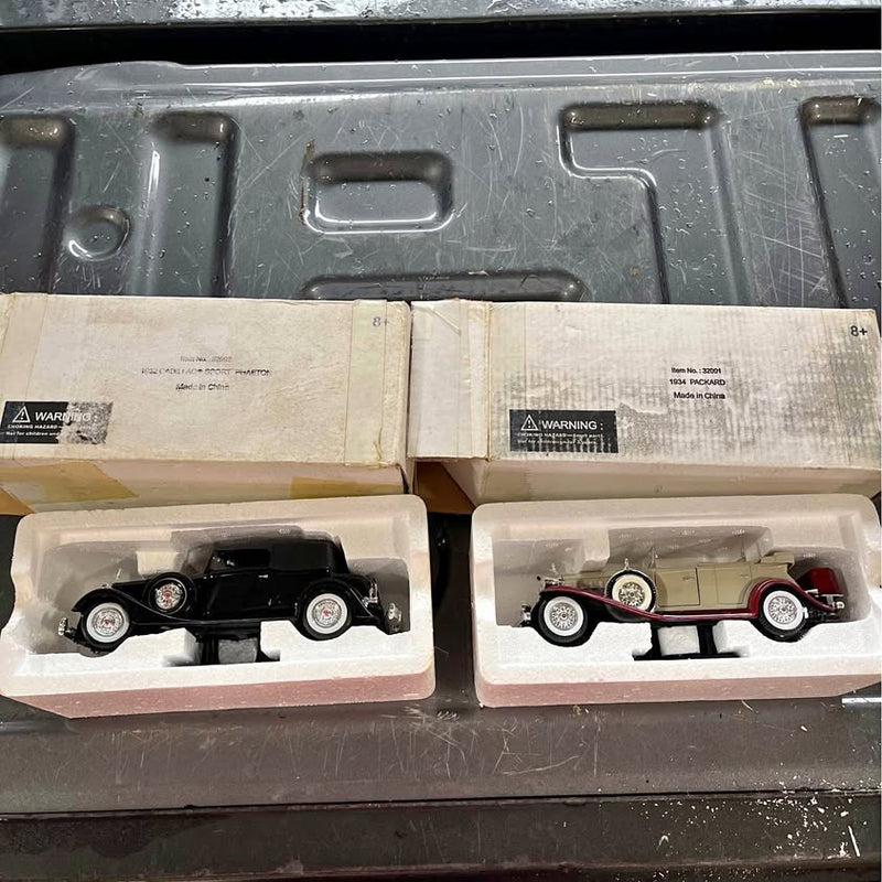 Diecast car model in box, black car with whitewall tires and red car in packaging