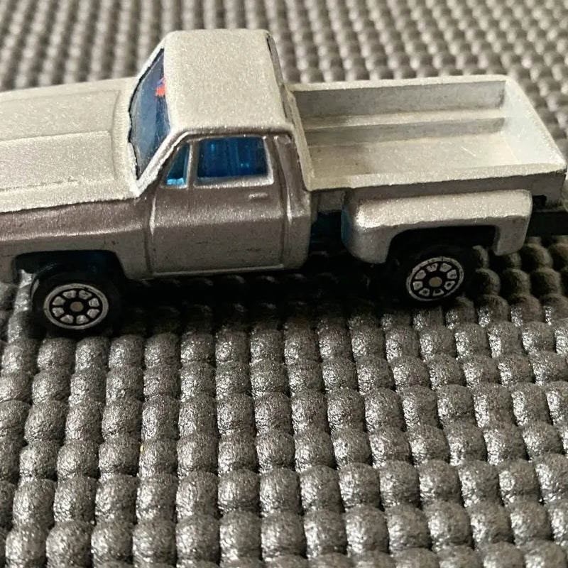 Vintage diecast pickup truck with silver-gray body and blue window cab