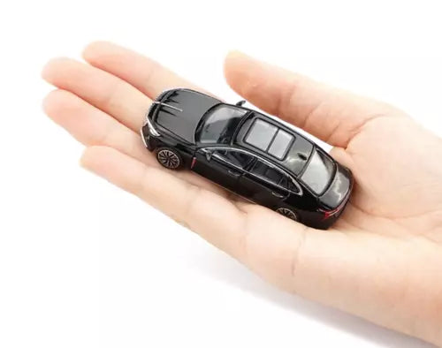 1:64 scale black diecast sedan model toy car in a hand, side view