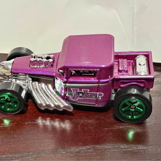 Purple diecast toy car with Joker graphic, silver engine, and green wheels