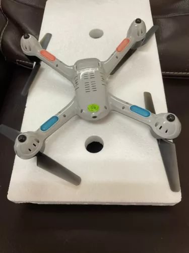 Grey quadcopter drone with four propeller arms, resting on box