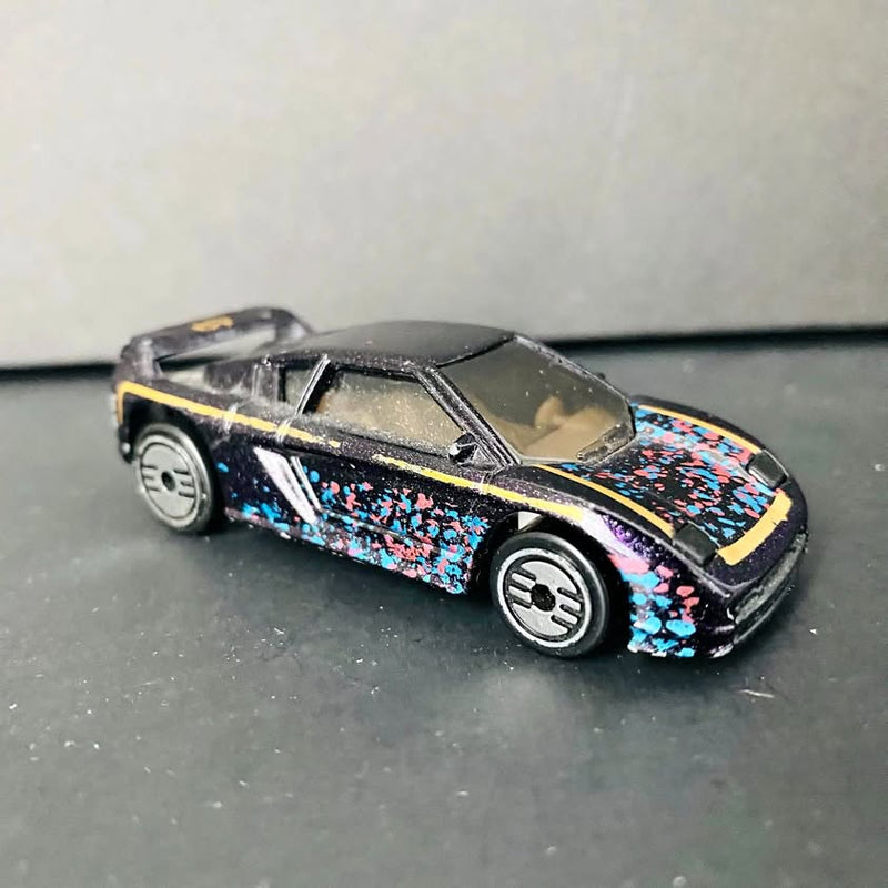 Diecast toy car with black body and multicolor speckled side panels, chrome wheels