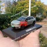 Silver diecast sedan model on dark base, held in hand, front three-quarter view