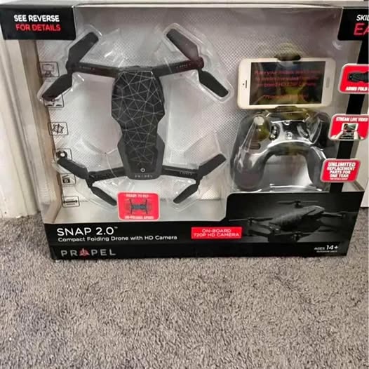 Folding quadcopter drone with controller inside retail box, visible prop arms and camera pod