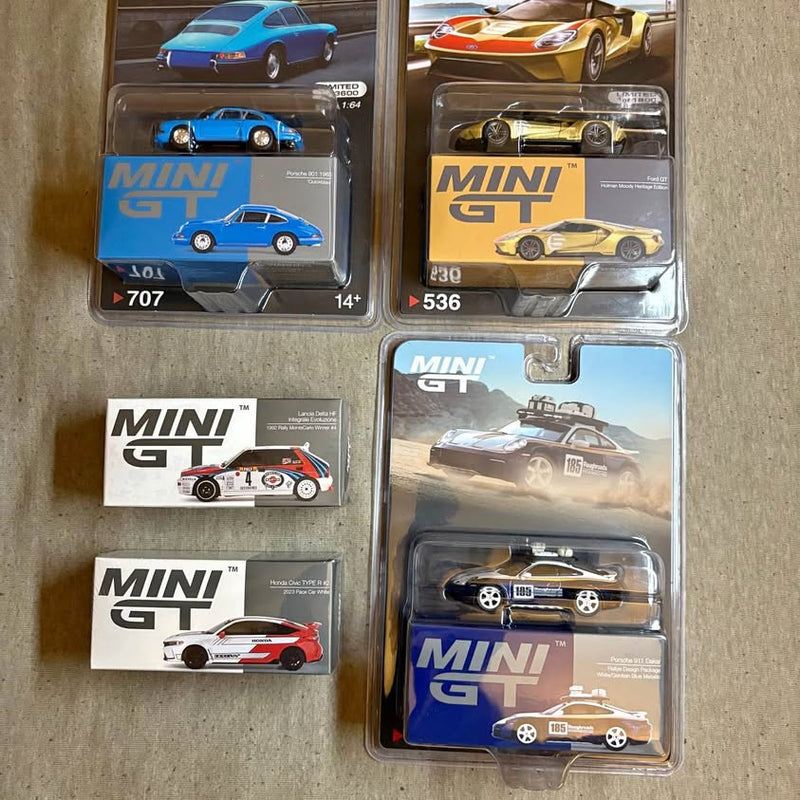 1/64 scale Mini GT diecast car in clear blister packaging, multiple cars shown