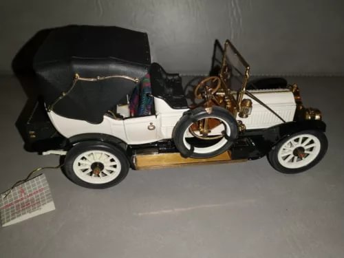 Vintage diecast car model with black hood, white body, gold trim, and white-spoke wheels.