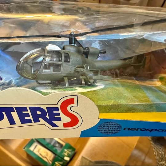 Green-gray diecast helicopter model with rotor and landing gear, in blister packaging