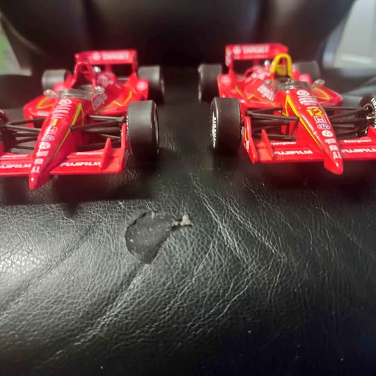 Red diecast race cars with front wings, front view on black surface