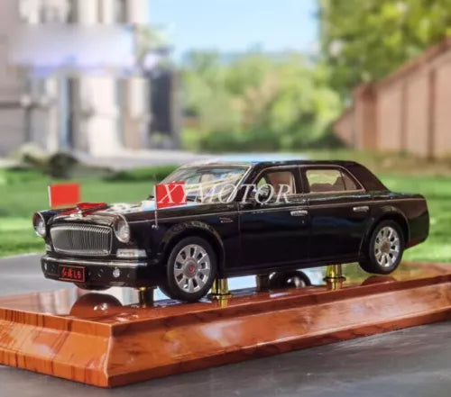 Black diecast model sedan car with chrome grille and red emblem, on wooden display base