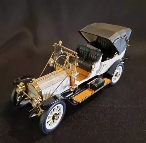 Diecast vintage car model with open top, white body, black fenders, gold details.