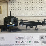 Black drone with camera lens and four propellers, on top of box inserts