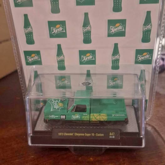 Diecast truck in clear display case, green soda-themed livery, on card tray