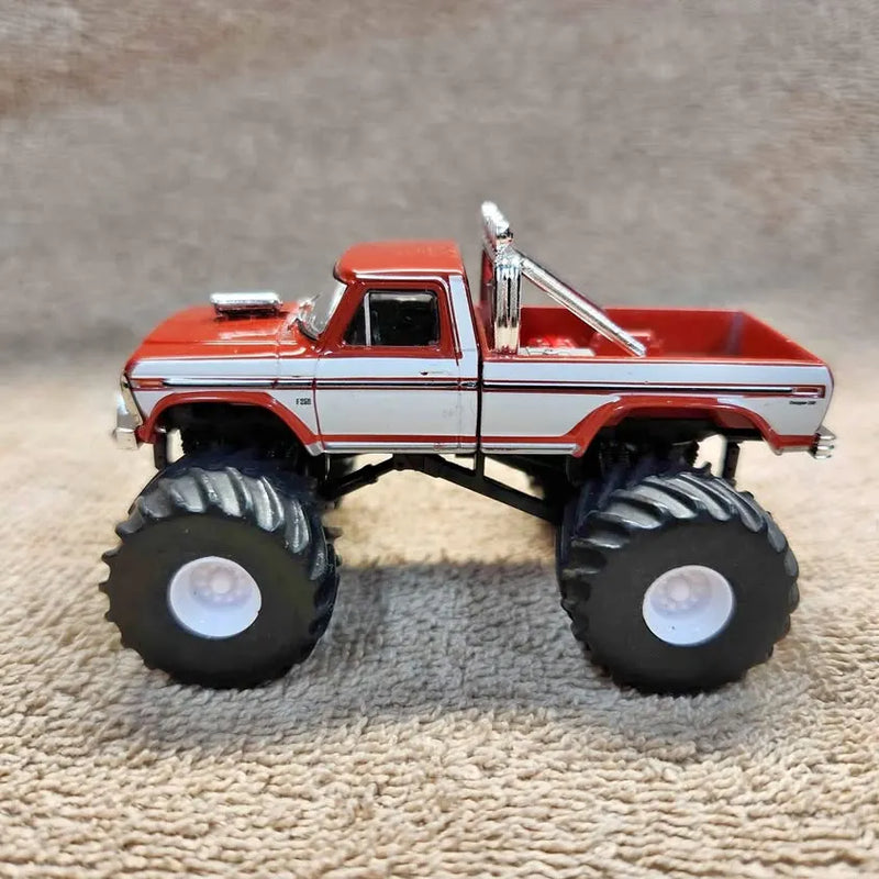 Red and white 1:64 diecast pickup truck with large black monster tires, side view