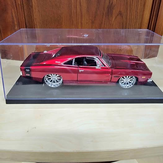 Maroon diecast model car with chrome wheels in clear display case on gray base