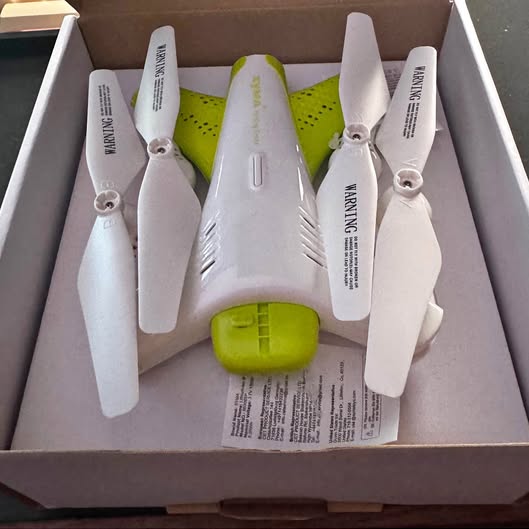 White quadcopter drone with four folding propellers and green battery pack