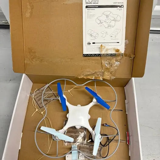 White quadcopter drone with blue propellers and controller wires in open box