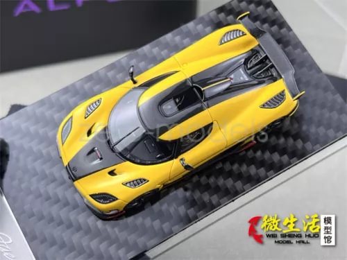 Yellow 1:64 sports model diecast car with rear wing on carbon-fiber display base