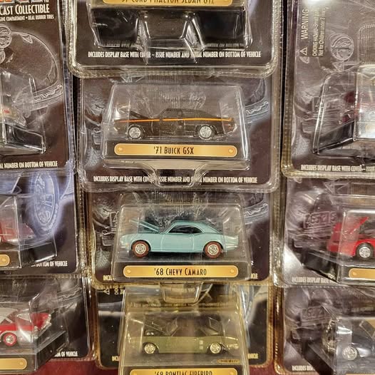 Diecast toy cars in clear boxes, teal 1968 Chevy Camaro and orange 1971 Buick GSX.