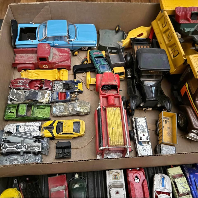 Vintage die-cast toy car lot with trucks and parts in cardboard box