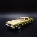 Die-cast model car of a 1976 yellow coupe with white roof, front three-quarter view