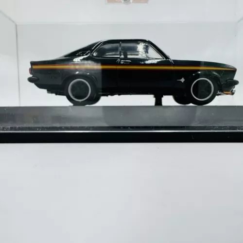 Black vintage die-cast coupe model car with gold stripe, side profile in display case