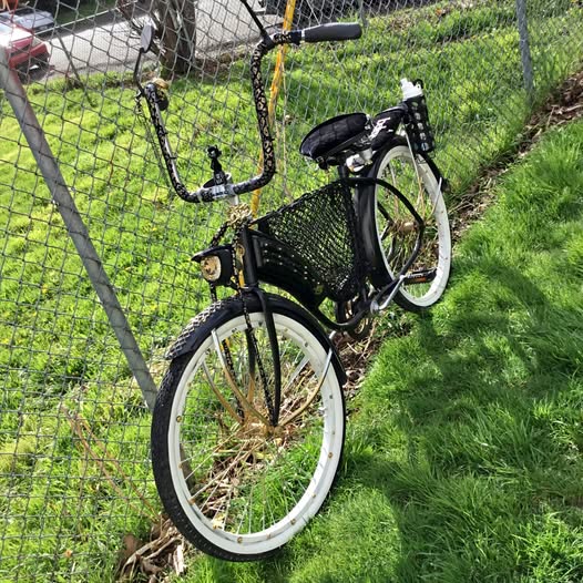 Black vintage bicycle with front wire basket and white tires behind a fence