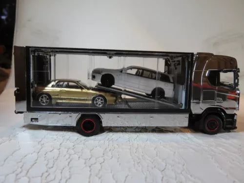 Diecast tow truck model with enclosed trailer, brown cab, exposed car inside.