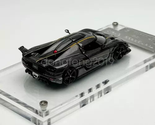1:64 diecast racing sports car model, black carbon-fiber look, gold accents, on base