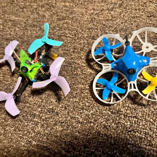 Tiny whoop quadcopter drones, green and blue with four propellers, on a surface