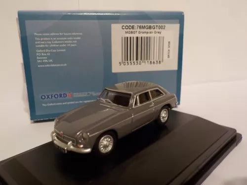 Grey diecast model car, front-left view on display base, with packaged box behind
