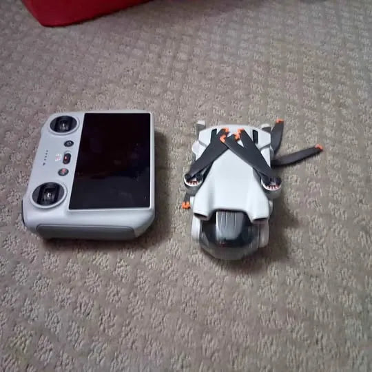 Foldable mini drone with RC remote controller, side-by-side on carpet