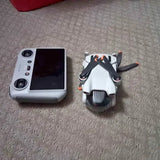 Foldable mini drone with RC remote controller, side-by-side on carpet