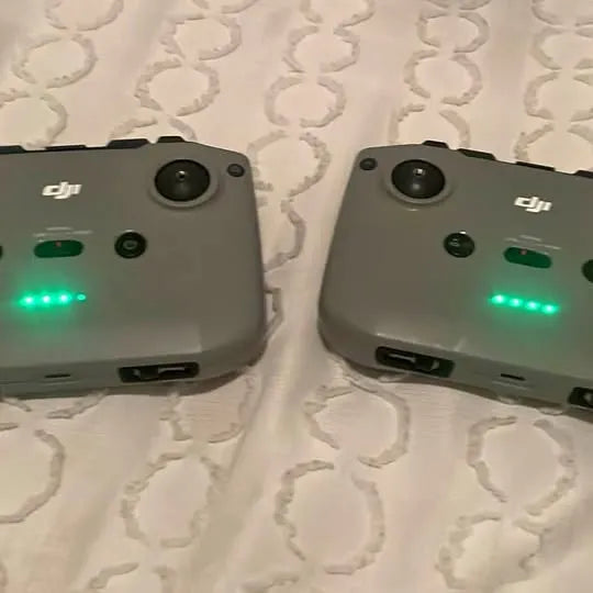 DJI Mini 2 drone controllers, two gray controllers with green LED indicators