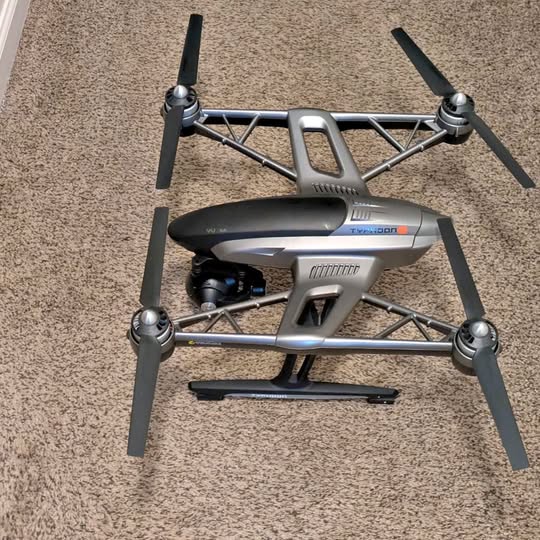 Foldable quadcopter drone with gray body and four propeller arms, on landing frame