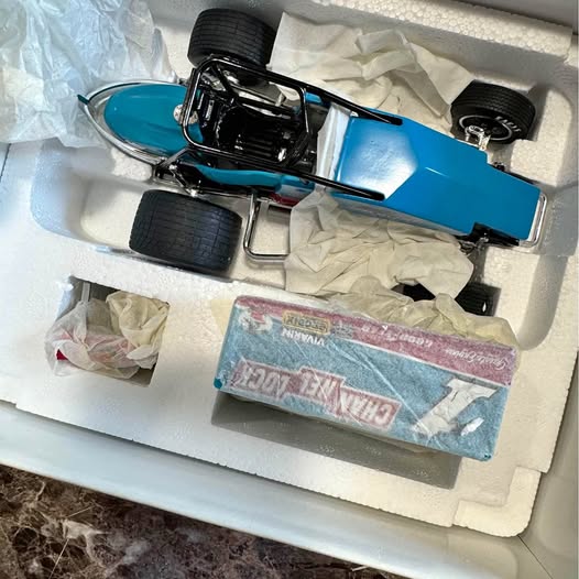 Blue diecast collectible car with black wheels and detailed chassis in a box