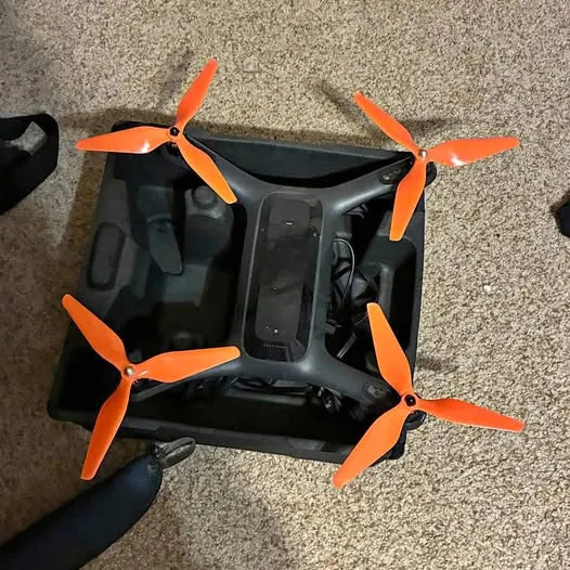 Black quadcopter drone with four orange propellers and center camera module