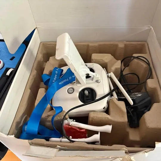 White quadcopter drone with propellers and camera, in box with blue strap