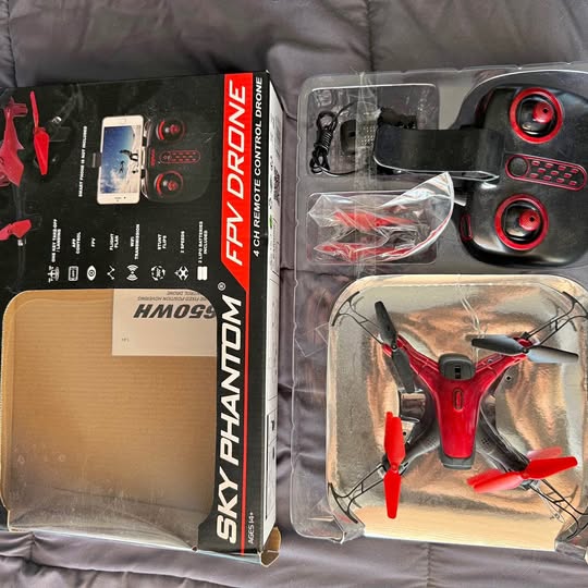 Red FPV drone with 4 propellers in clear retail box, accessories bag included