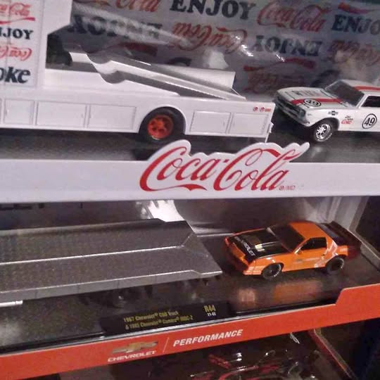 Orange diecast Camaro on Coca-Cola hauler display with gray track and perforated base