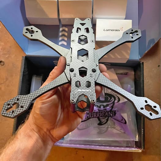 Metal drone frame plate with cutouts, held in hand; cross-shaped arms