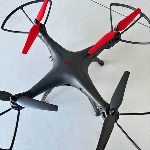 Black quadcopter drone with red propeller blades and four arms