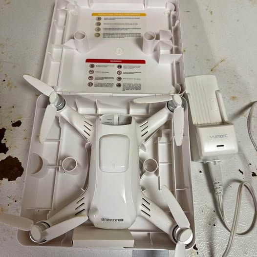 White quadcopter drone with four propellers, shown in open box