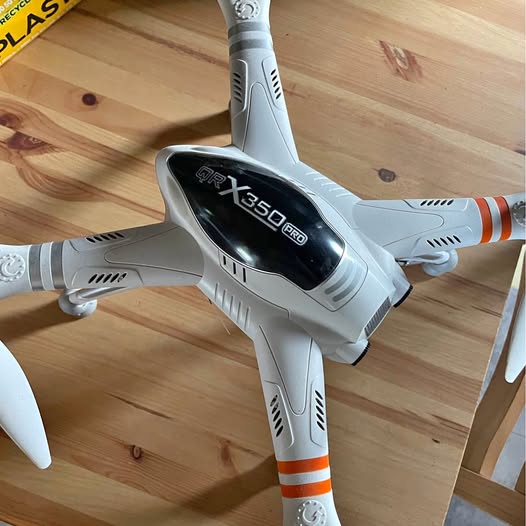 Drone quadcopter in light gray with black front screen and orange stripe accents