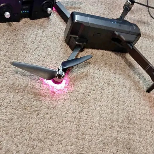 Gray quadcopter drone with two visible propellers and pink under-light