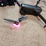 Gray quadcopter drone with two visible propellers and pink under-light