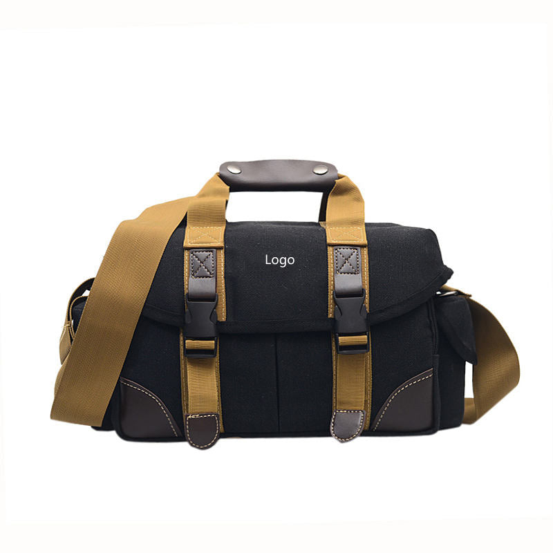Black canvas sling camera carry case with front flap, tan straps, buckle closures, logo patch