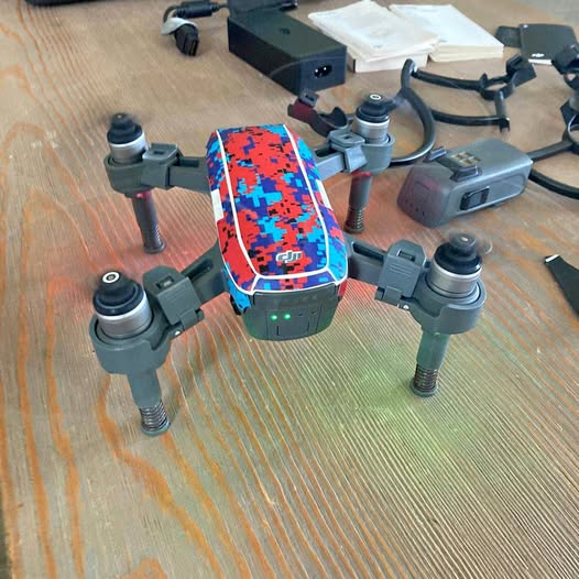 Camouflage quadcopter drone with four arms and propellers, front control screen