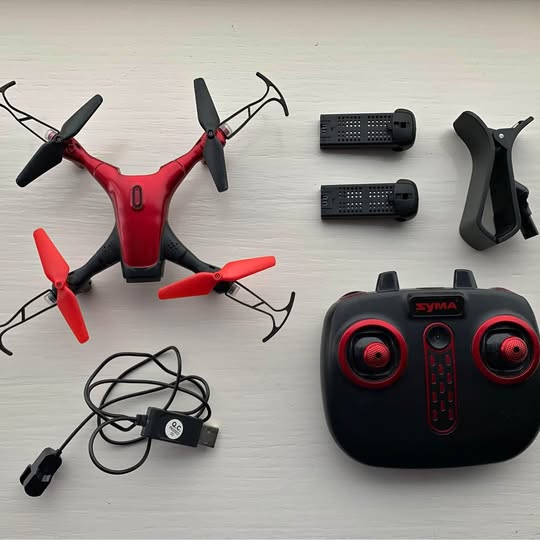 Red and black quadcopter drone with remote controller and power cable.