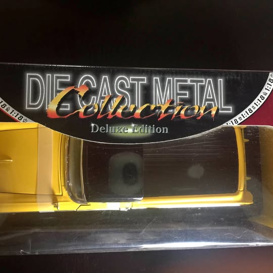Yellow diecast car model in retail box, front view with clear window